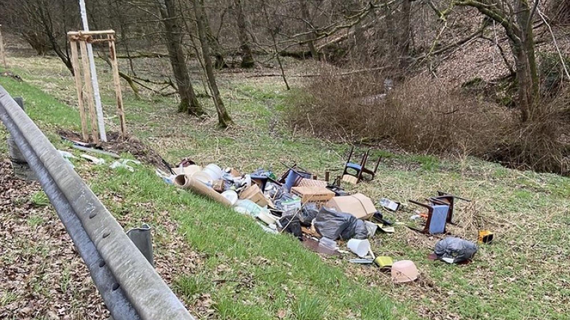 Ein Sperrmüllhaufen liegt auf einer Wiese hinter einer Leitplanke.