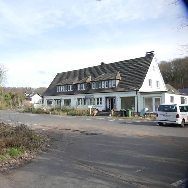 Das geschlossene Restaurant Kavala in Lohmar-Donrath: Ein weißes Haus mit Spitzdach und gauben, davor ein leerer Parkplatz. Unkraut wächst und Müll liegt an der Treppe.