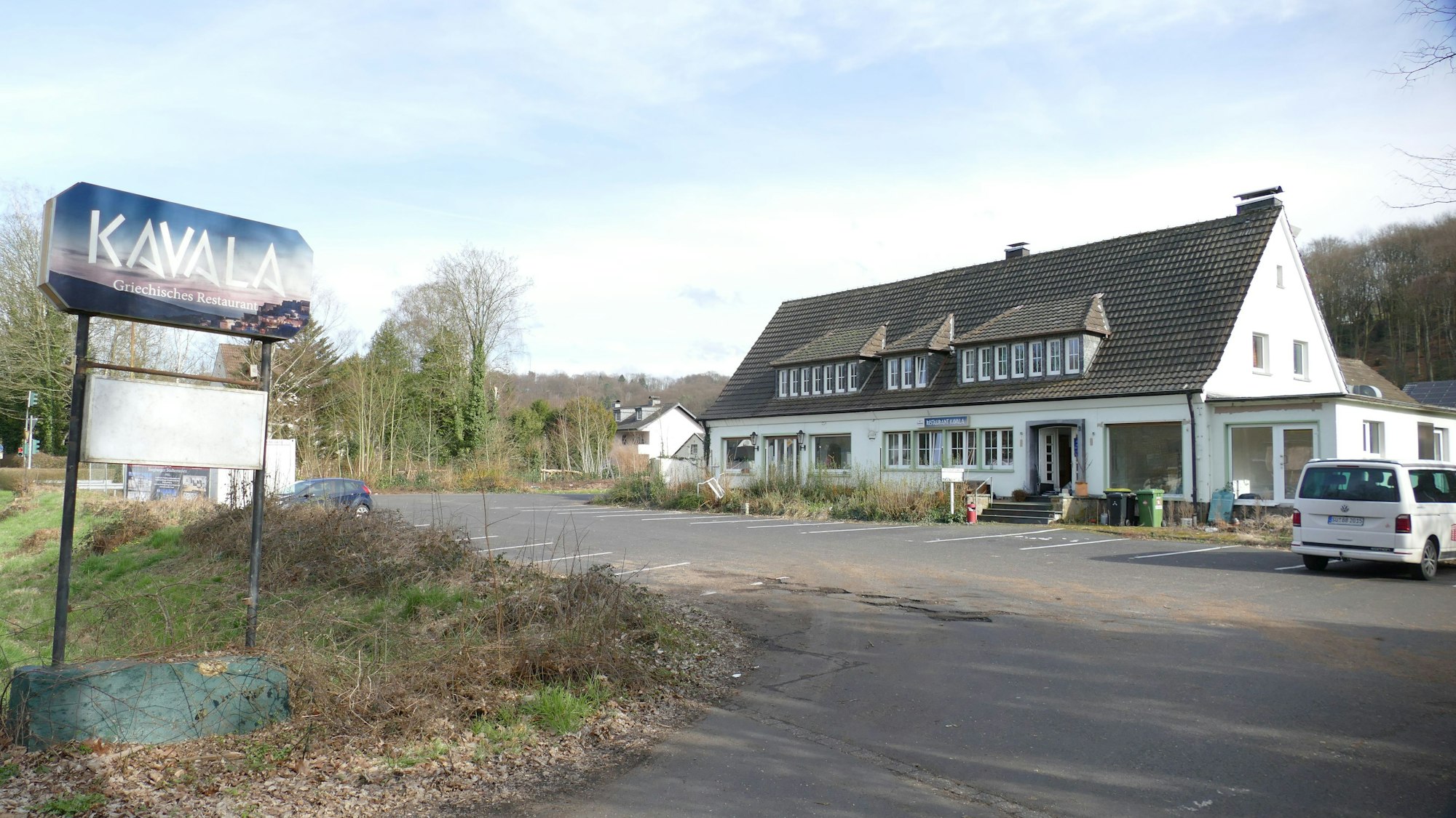 Das geschlossene Restaurant Kavala in Lohmar-Donrath: Ein weißes Haus mit Spitzdach und gauben, davor ein leerer Parkplatz. Unkraut wächst und Müll liegt an der Treppe.