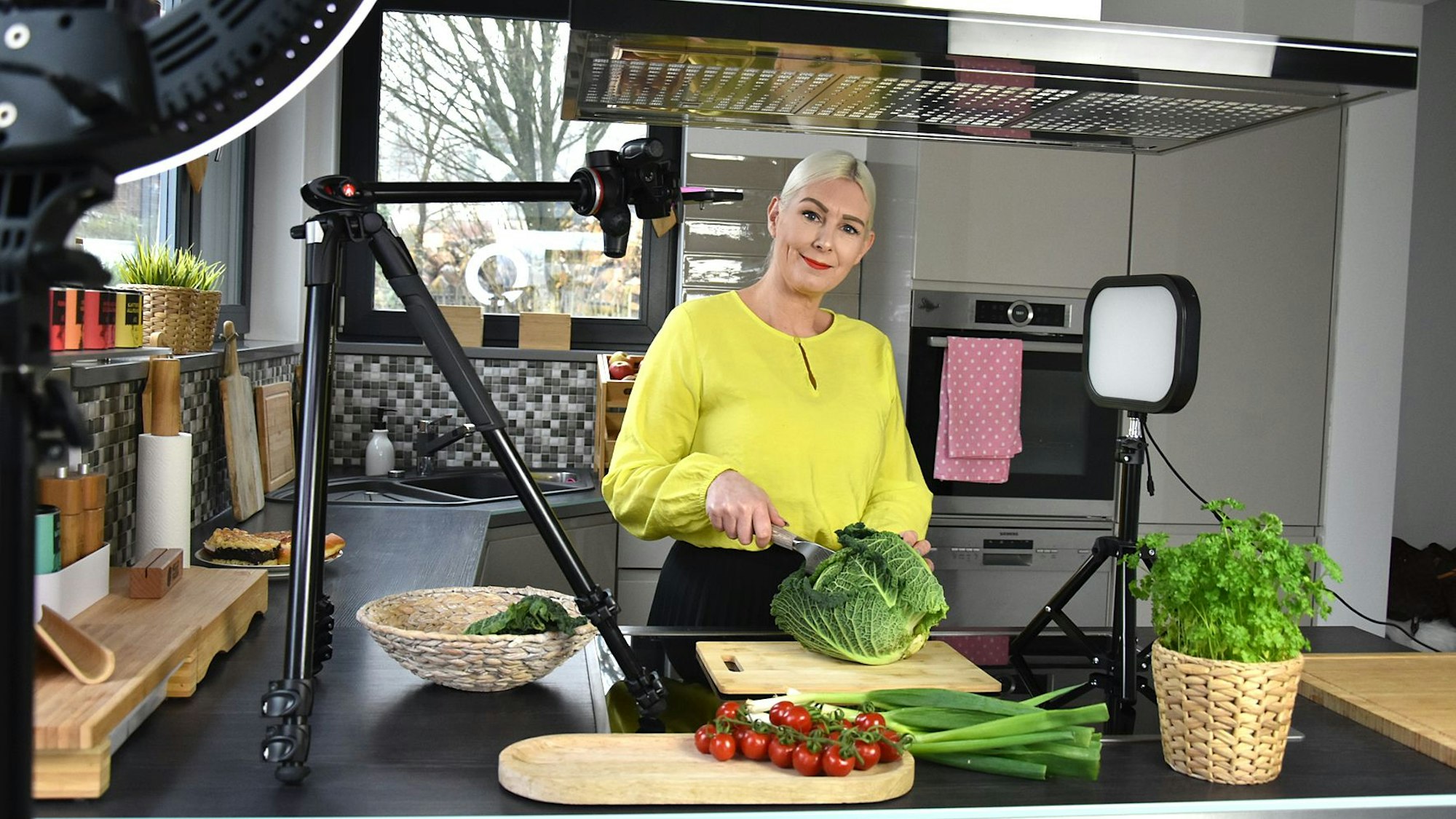 Sandra Franitza steht in einer Küche und lächelt in die Kamera, während sie einen Salatkopf schneidet.