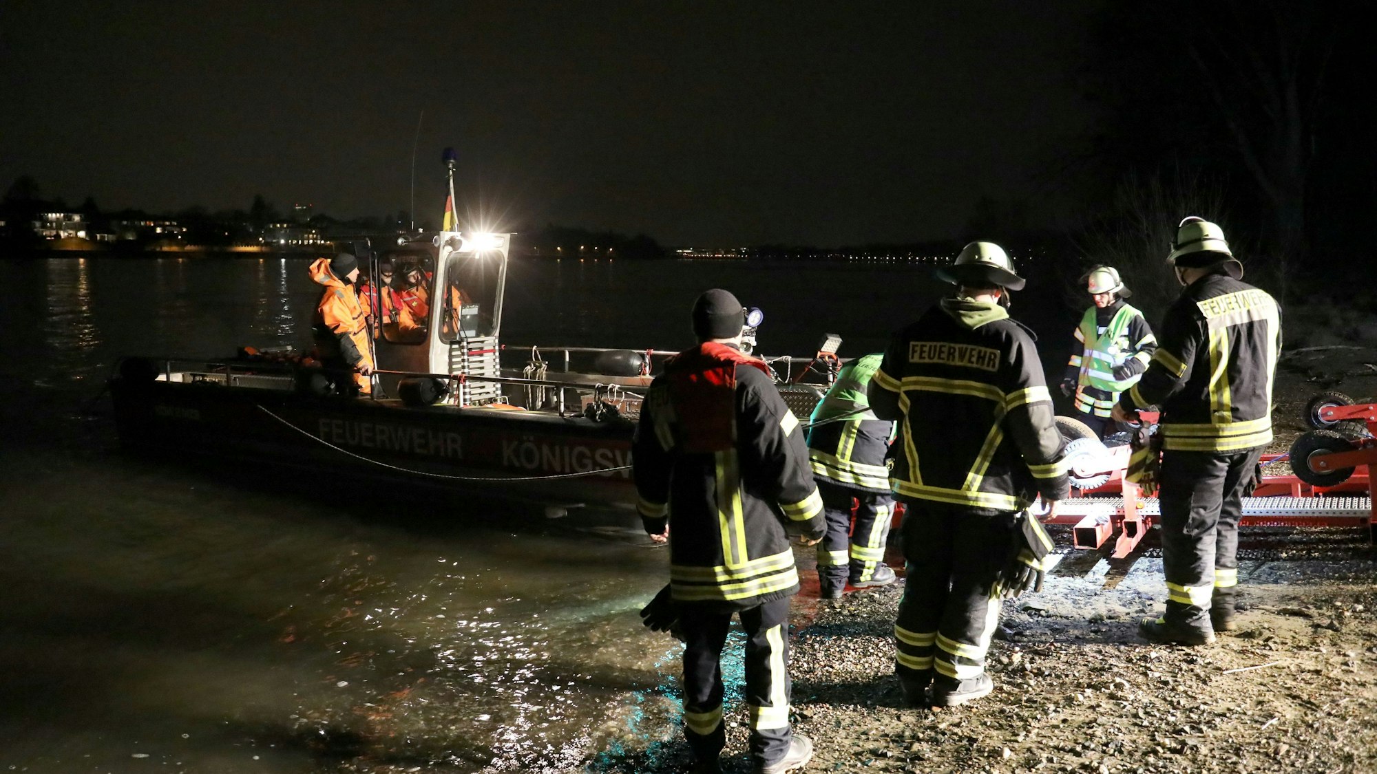 Mehrere Mitarbeiter der Feuerwehr stehen am Ufer des Rheins.