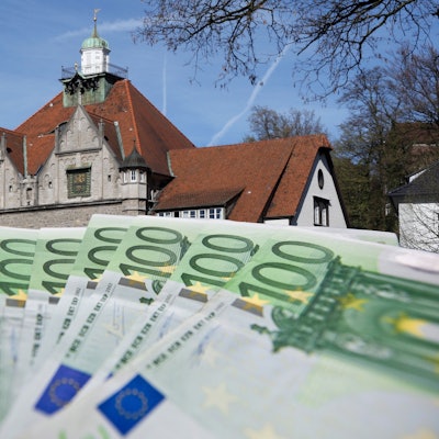 Geldscheine werden aufgefächert vor das Rathaus in Bergisch Gladbach gehalten.