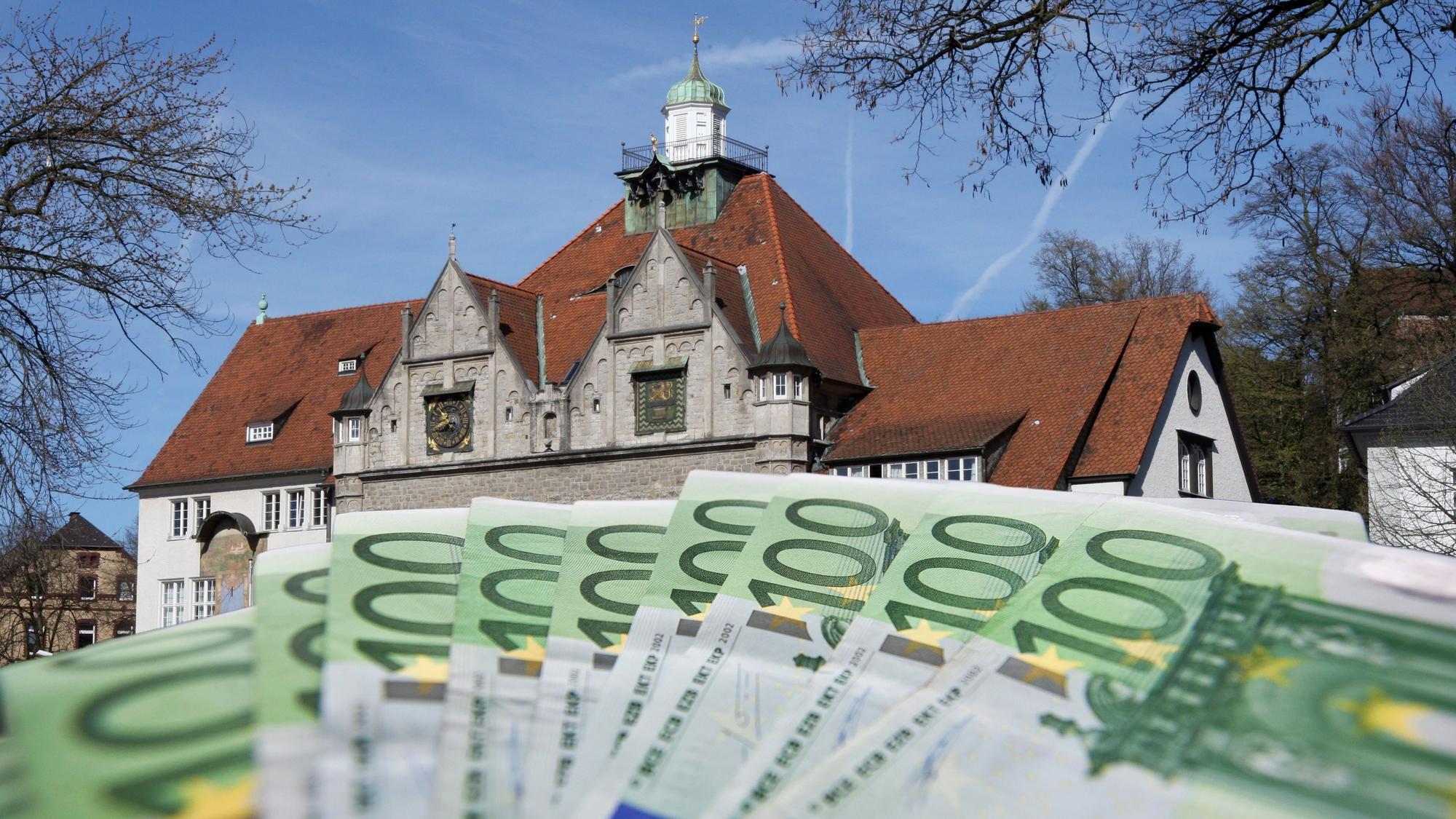 Fotomontage zeigt Geldscheine im Vordergrund, das Rathaus im Hintergrund.