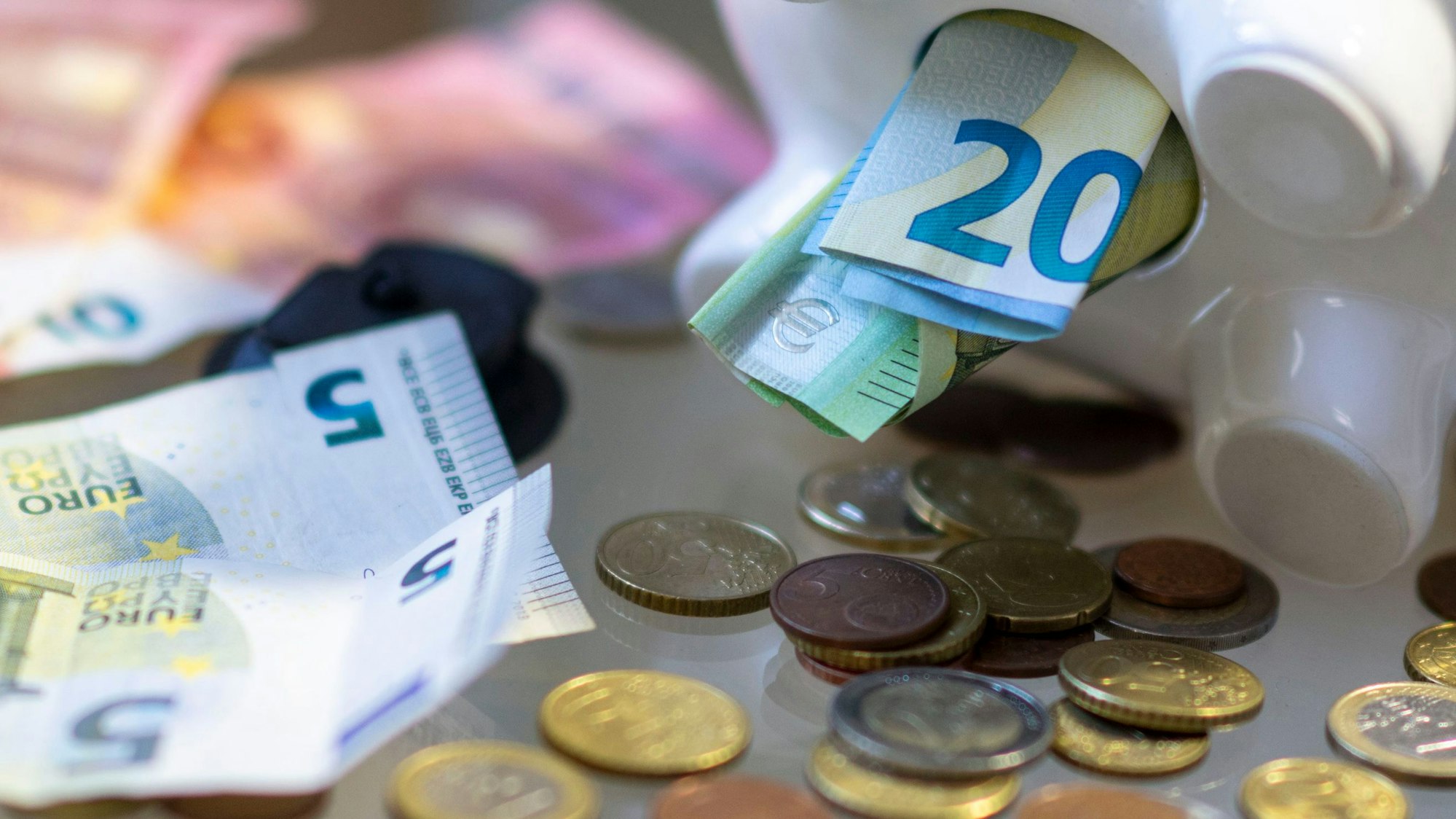 Aus dem Bauch eines Sparschweins kommen Geldscheine und Münzen.