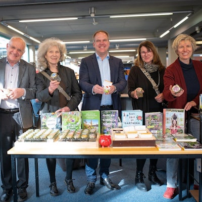 Drei Frauen und drei Männer lächeln in die Kamera, sie stehen hinter einem Tisch, auf dem Saatgut liegt.