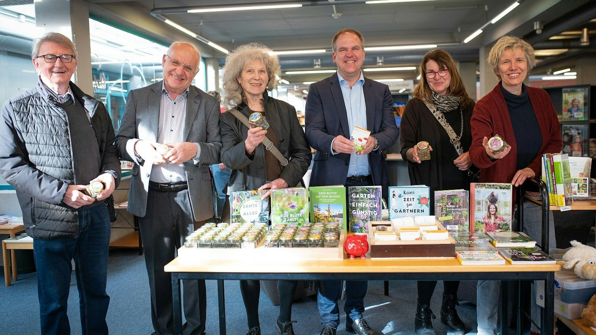 Drei Frauen und drei Männer lächeln in die Kamera, sie stehen hinter einem Tisch, auf dem Saatgut liegt.