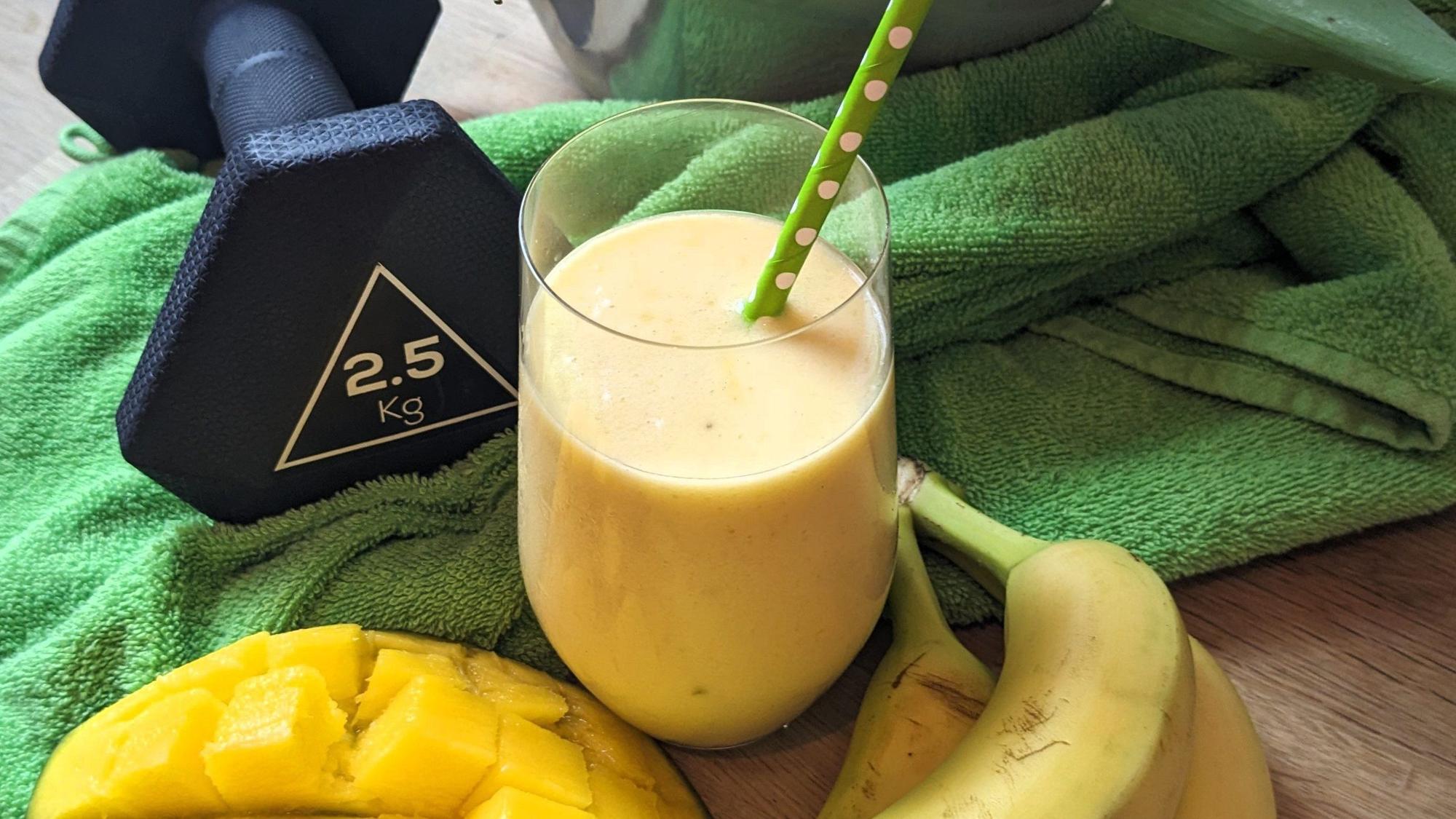 Ein Glas ist mit der Fruchtbuttermilch gefüllt. Davor liegen Banannen und eine halbe Mango.