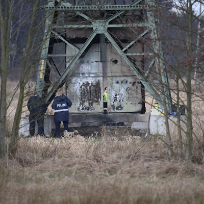 Polizisten ermitteln an einem beschädigten Strommasten auf einem Feld.