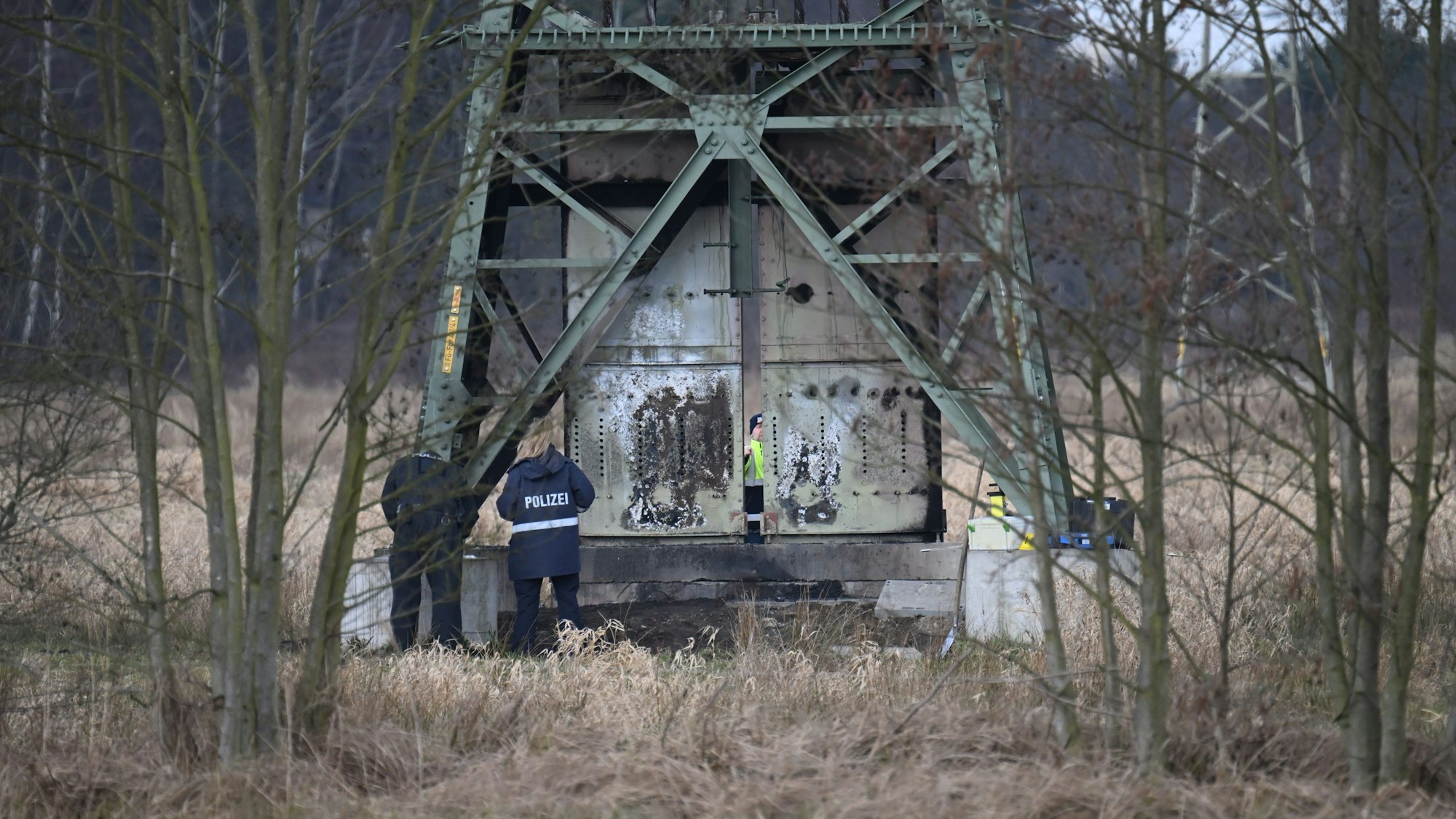 Polizisten ermitteln an einem beschädigten Strommasten auf einem Feld.
