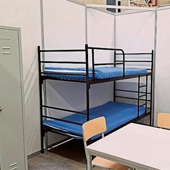 Rund zwei Meter hohe Wände schirmen zwei Etagenbetten, einen Tisch mit Stühlen und einen Schrank ab.