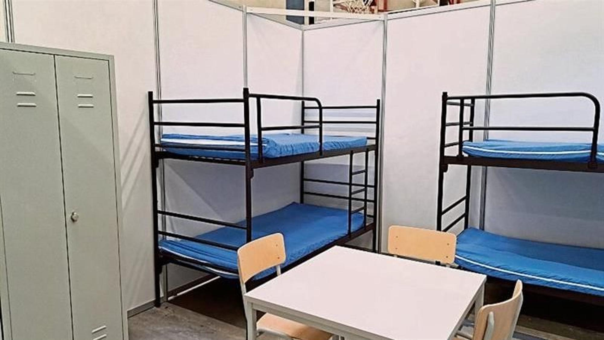 Rund zwei Meter hohe Wände schirmen zwei Etagenbetten, einen Tisch mit Stühlen und einen Schrank ab.