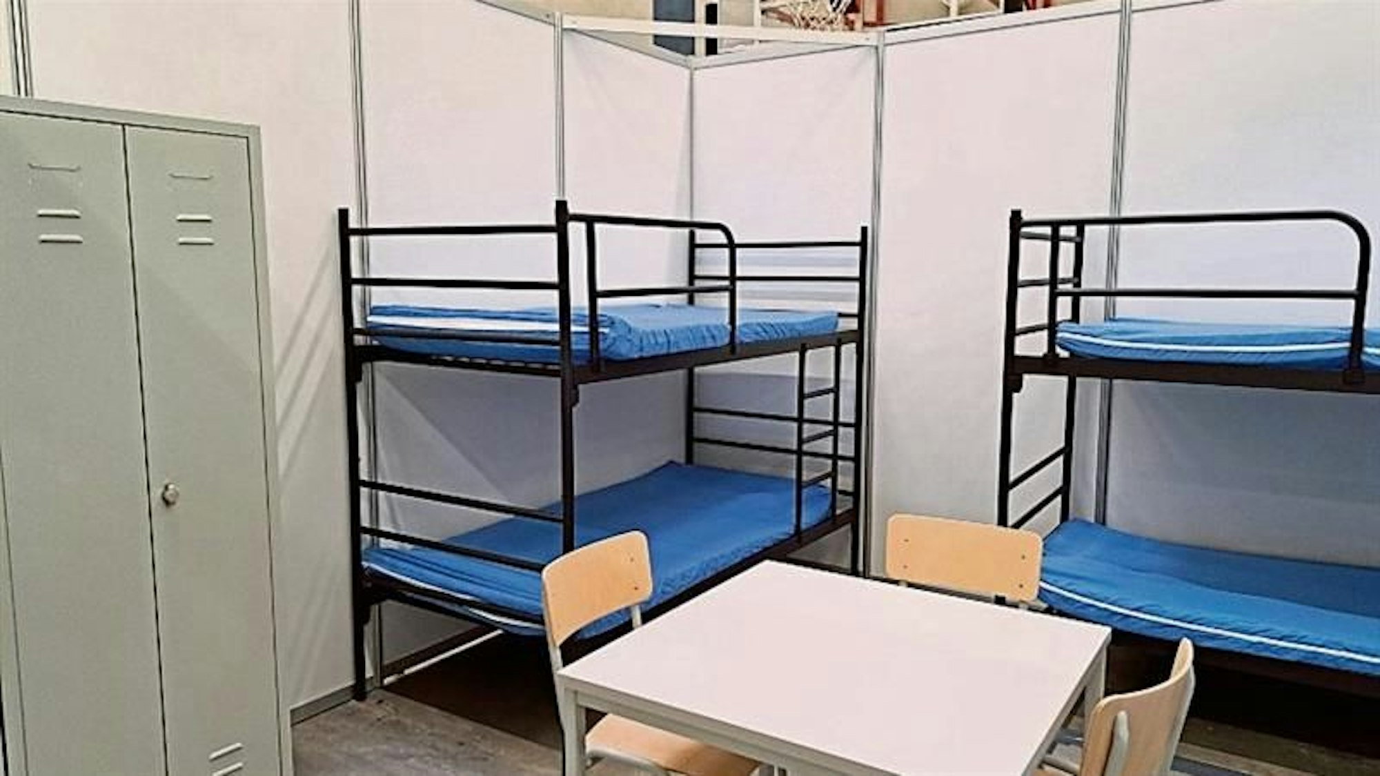 Rund zwei Meter hohe Wände schirmen zwei Etagenbetten, einen Tisch mit Stühlen und einen Schrank ab.