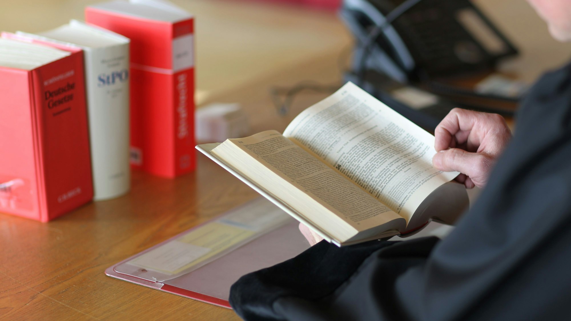 Hände, die ein aufgeschlagenes Gesetzbuch halten. Symbolbild