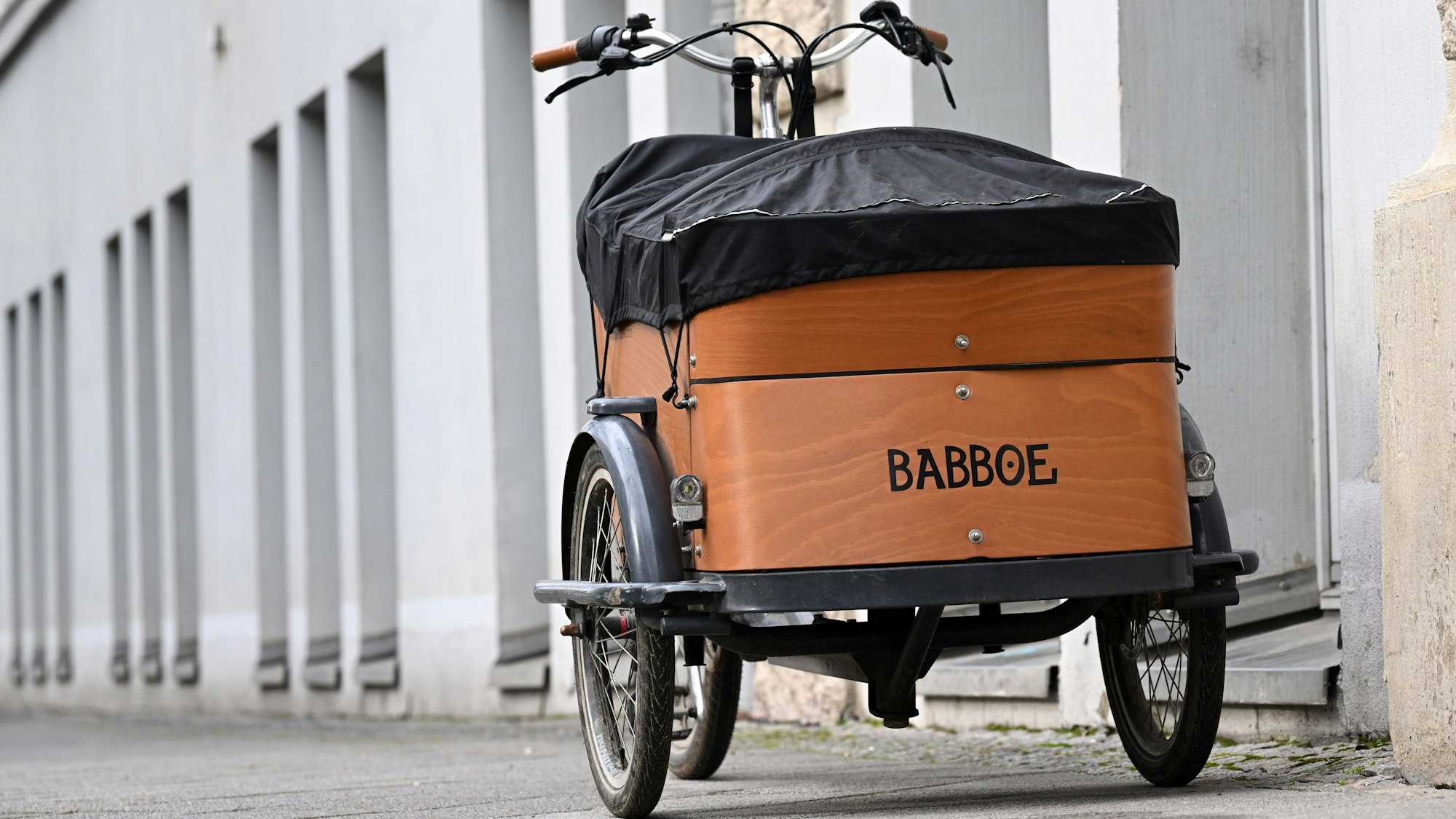 Ein Babboe-Lastenfahrrad parkt auf einem Bürgersteig neben einer Häuserfassade.