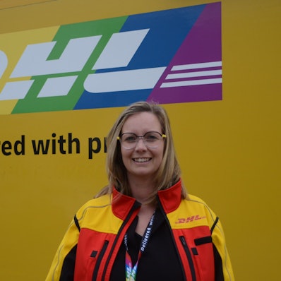 Eine blonde Frau in einer gelben Jacke mit DHL-Logo.