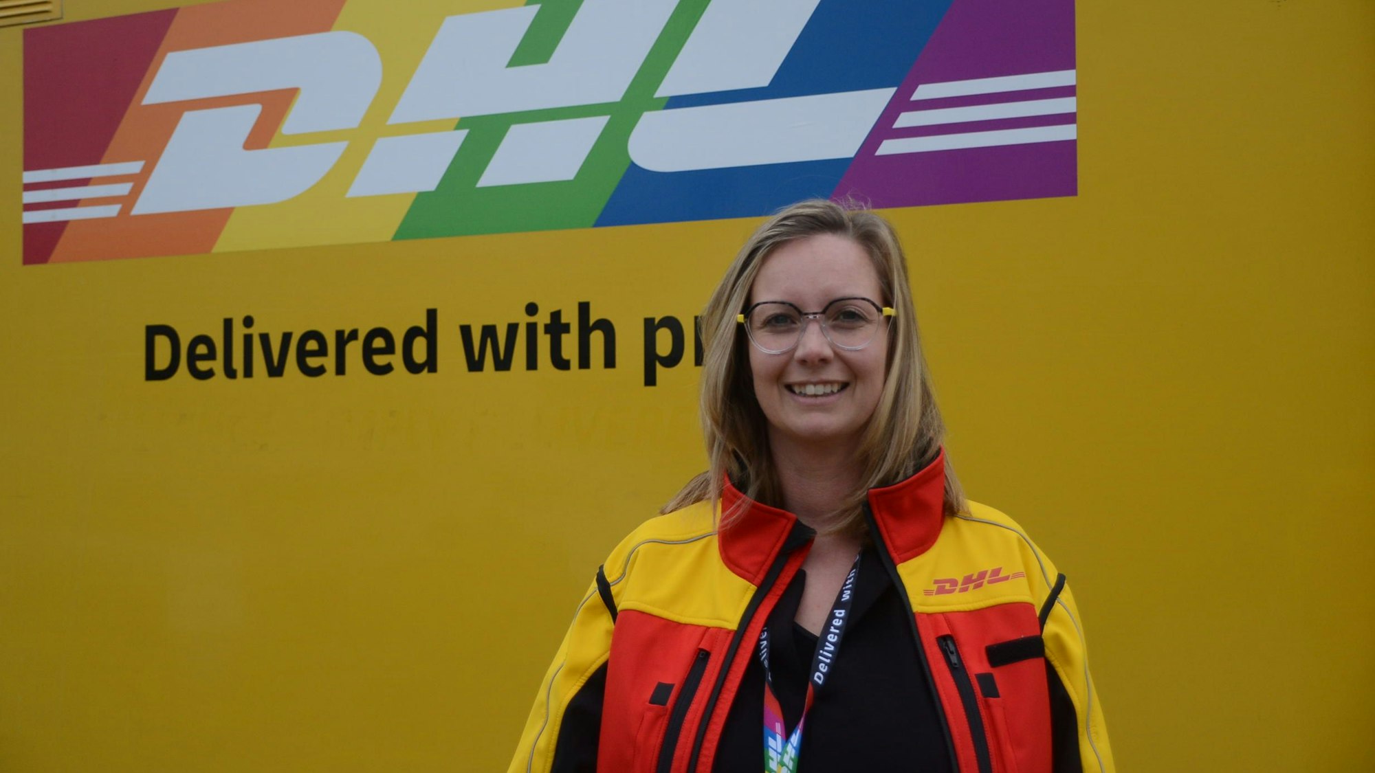 Eine blonde Frau in einer gelben Jacke mit DHL-Logo.