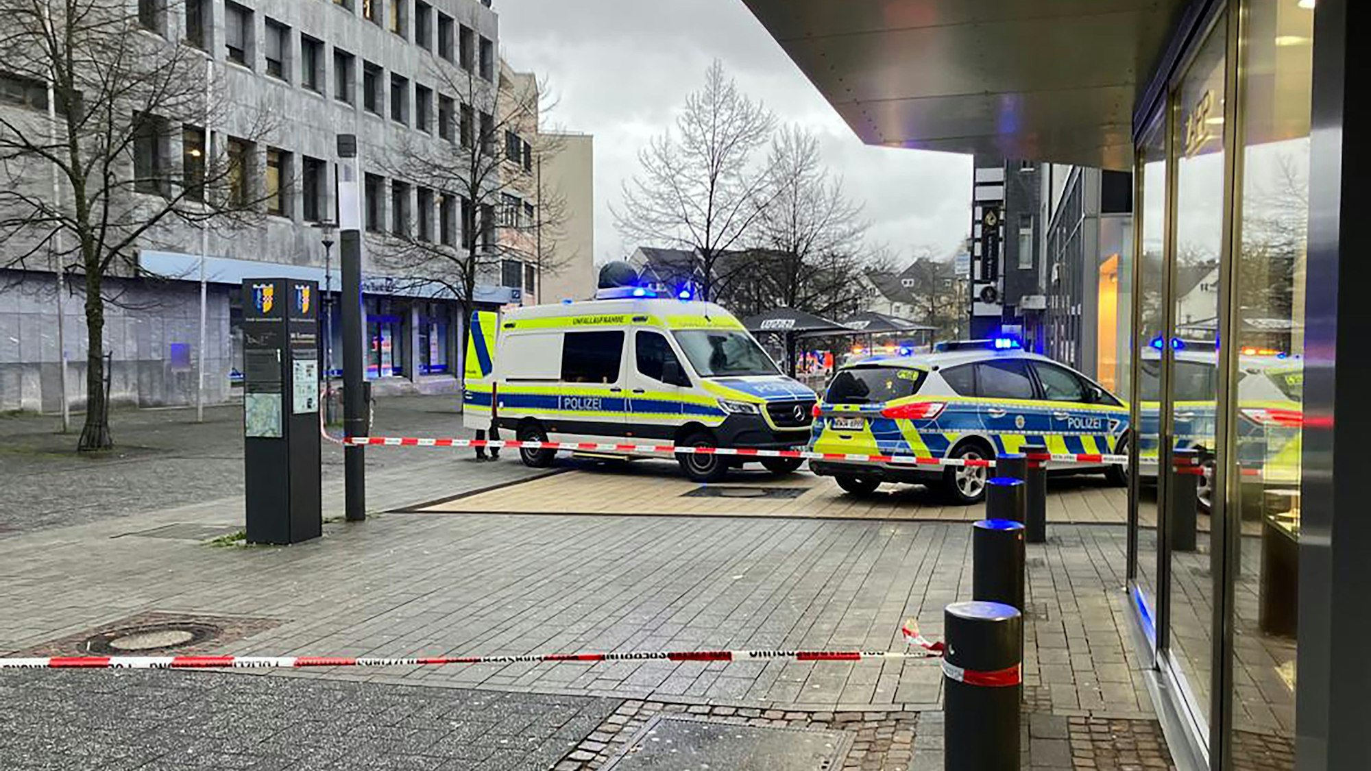 Zwei Polizeiautos stehen vor einem Bankgeschäft. Davor ist ein Tatport mit Flatterband abgesperrt worden.