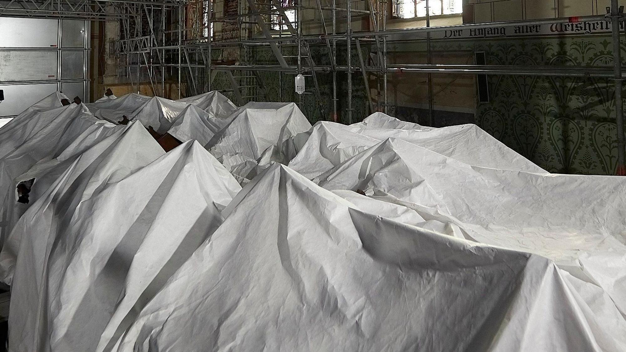 Weiße Laken dominieren das Bild. Zu erkennen sind die Konturen der Kirchenbänke, die mit den Laken abgedeckt sind.