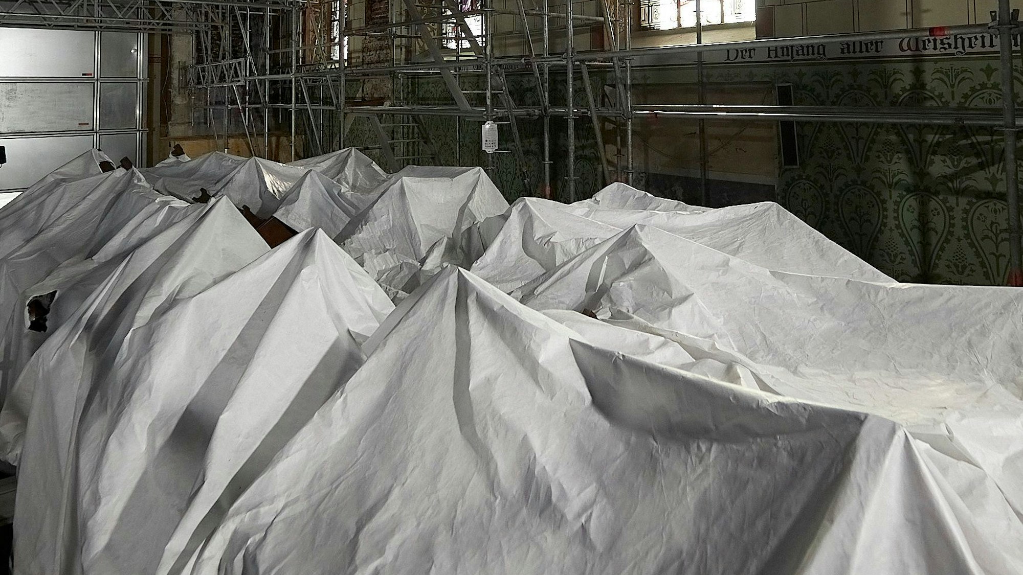 Weiße Laken dominieren das Bild. Zu erkennen sind die Konturen der Kirchenbänke, die mit den Laken abgedeckt sind.