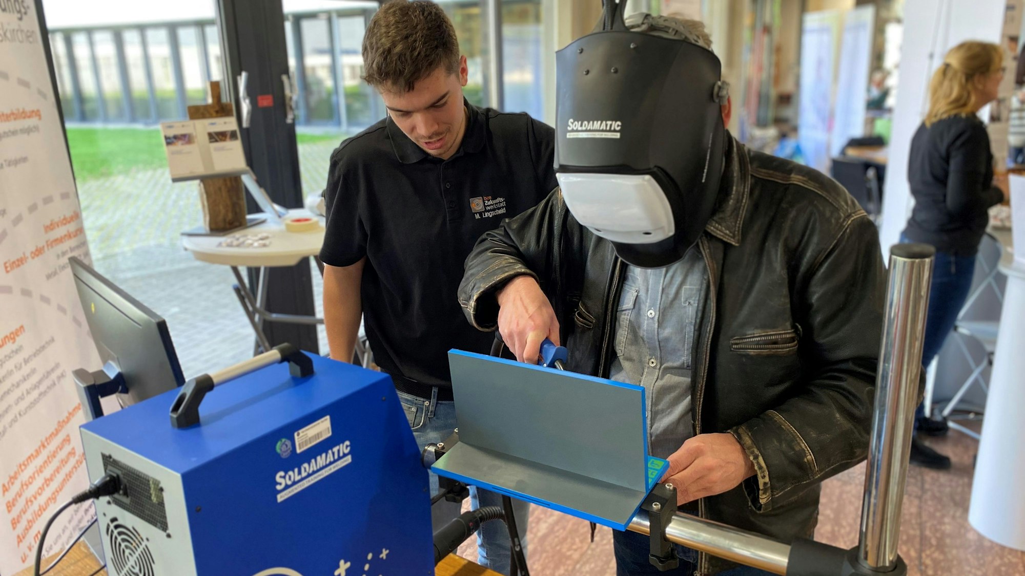 Ein älterer Mann arbeitet am Schweißgerät, ein jüngerer instruiert ihn.