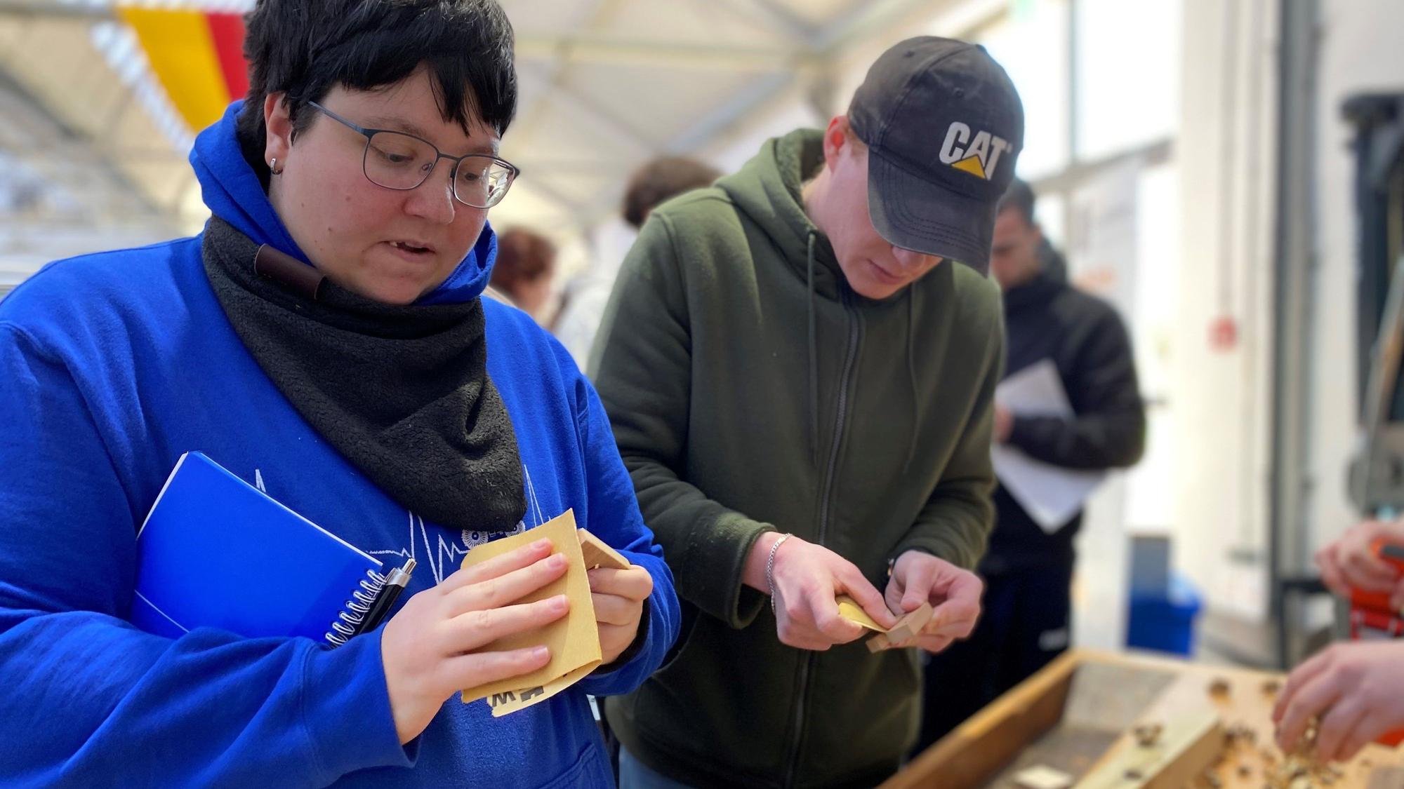Bei der Berufswahlmesse probieren eine Besucherin und ein Besucher den Bau einer Handyhalterung aus.