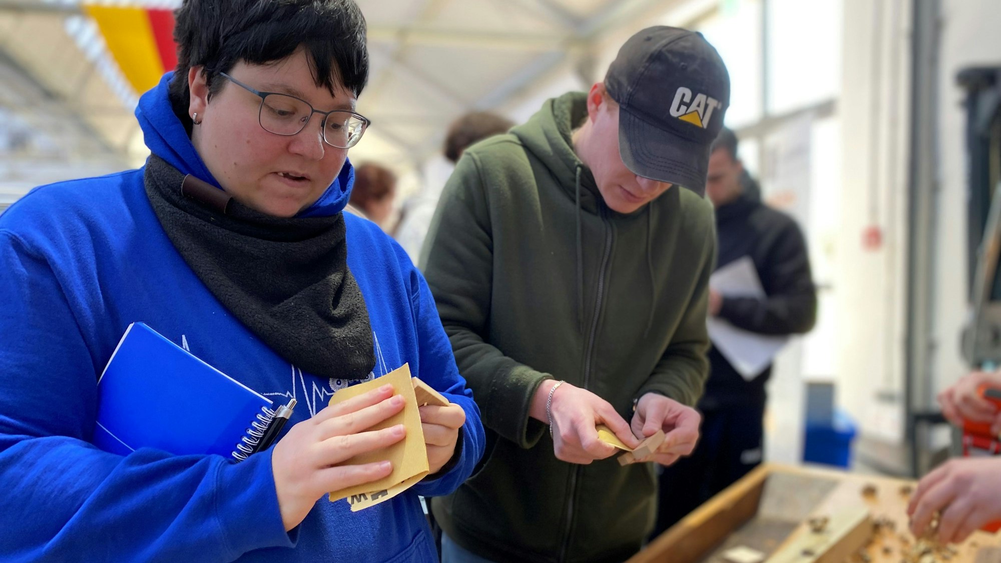 Bei der Berufswahlmesse probieren eine Besucherin und ein Besucher den Bau einer Handyhalterung aus.
