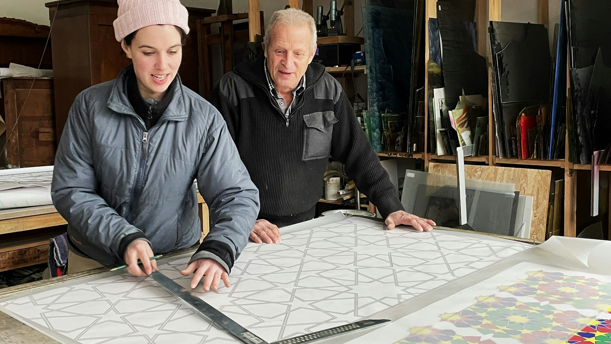 Junge Frau mit Mütze mit Mann an einem Tisch in der Glaswerkstatt
