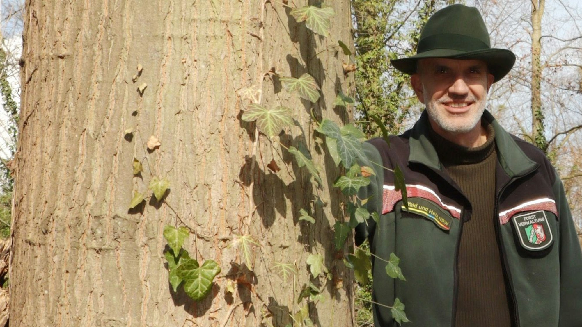 Zu sehen ist der Förster neben einem mächtigen Baum.