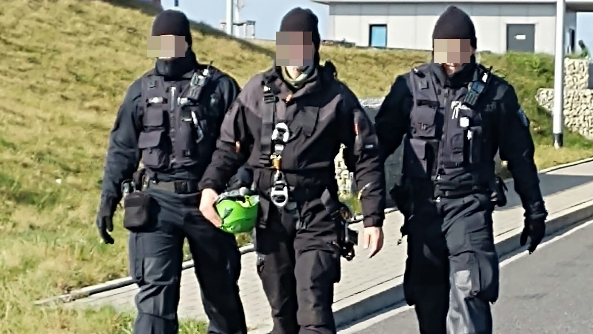 Der Greenpeace-Aktivist, der einen grünen Helm in der rechten Hand hält, lässt sich ohne Widerstand von den Polizeibeamten abführen.
