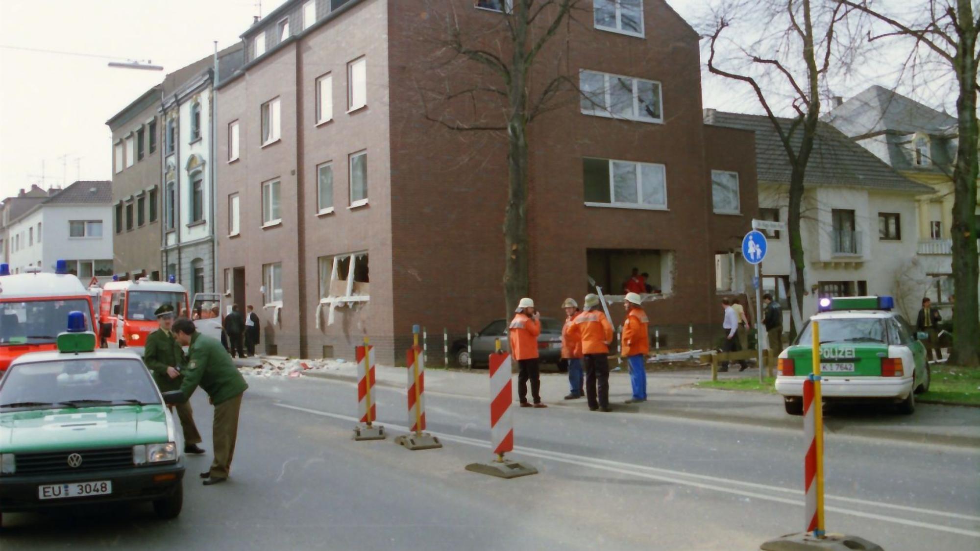 Das Bild zeigt im Hintergrund das Loch in der Fassade, das die Detonation verursacht hatte. Im Vordergrund sind zahlreiche Einsatzkräfte zu sehen.