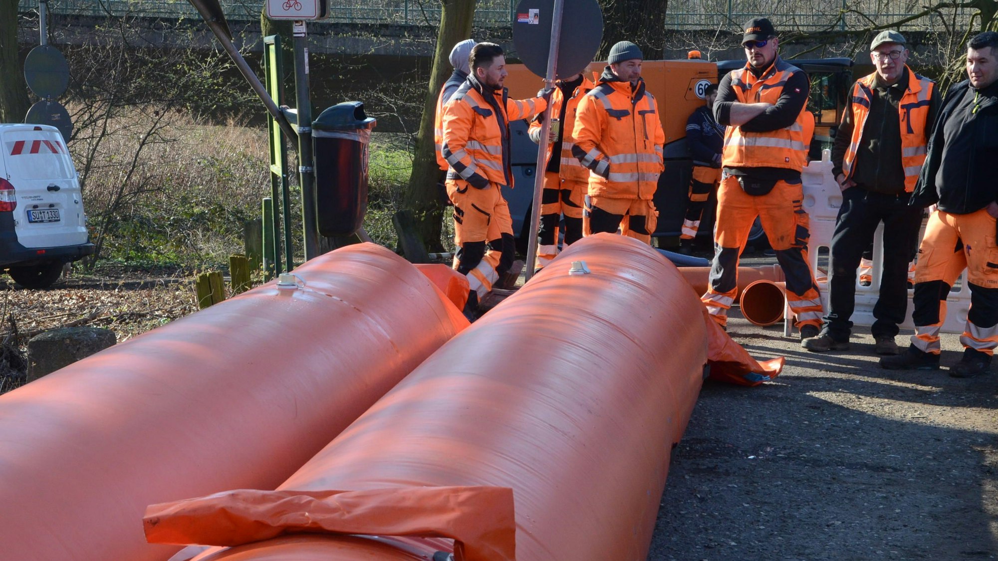 Männer in orange Arbeitsjacken stehen an der Einsatzstelle.