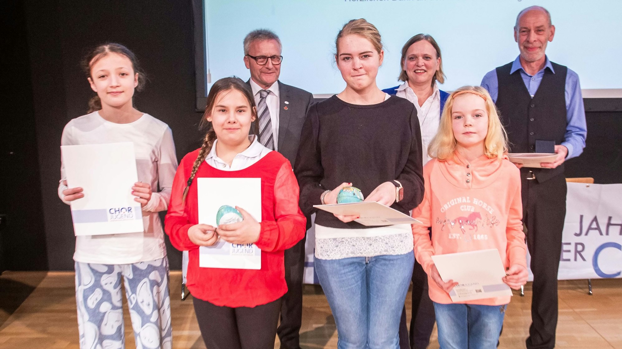 Vier Mädchen stehen in einer Reihe, sie halten Urkunden in den Händen. Hinter ihnen stehen zwei Männer und eine Frau.