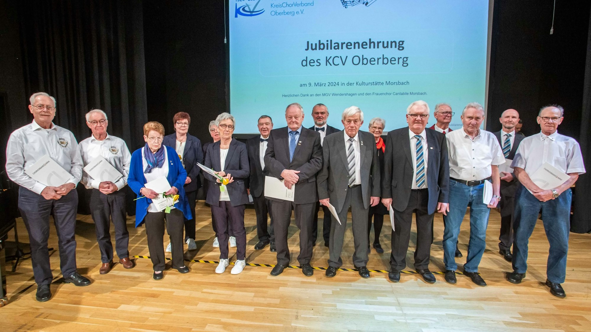 Eine Gruppe Männer und Frauen stehen in einer Reihe. Alle halten eine Urkunde in den Händen.