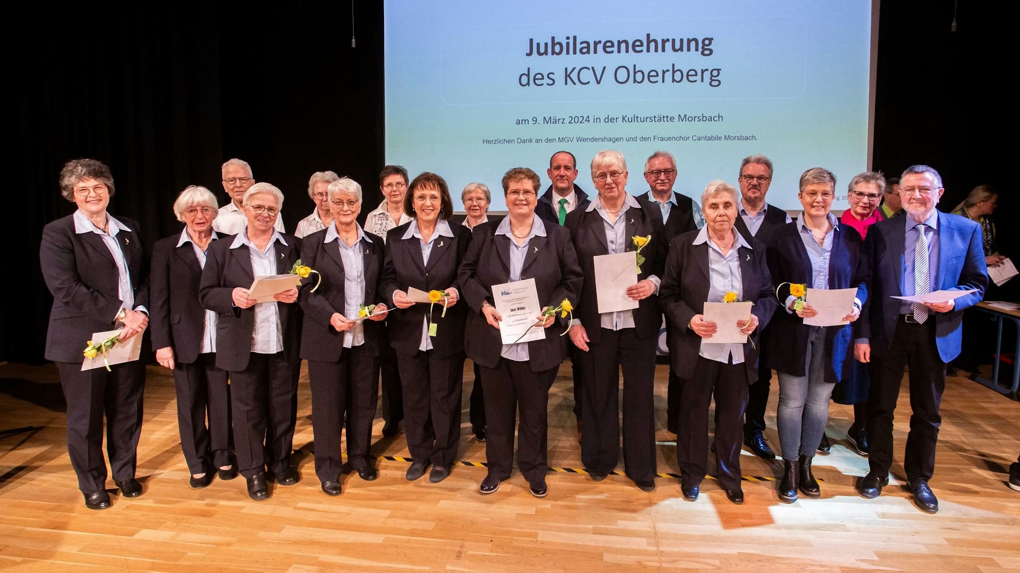 Eine Gruppe Männer und Frauen stehen in einer Reihe. Alle halten eine Urkunde in den Händen.