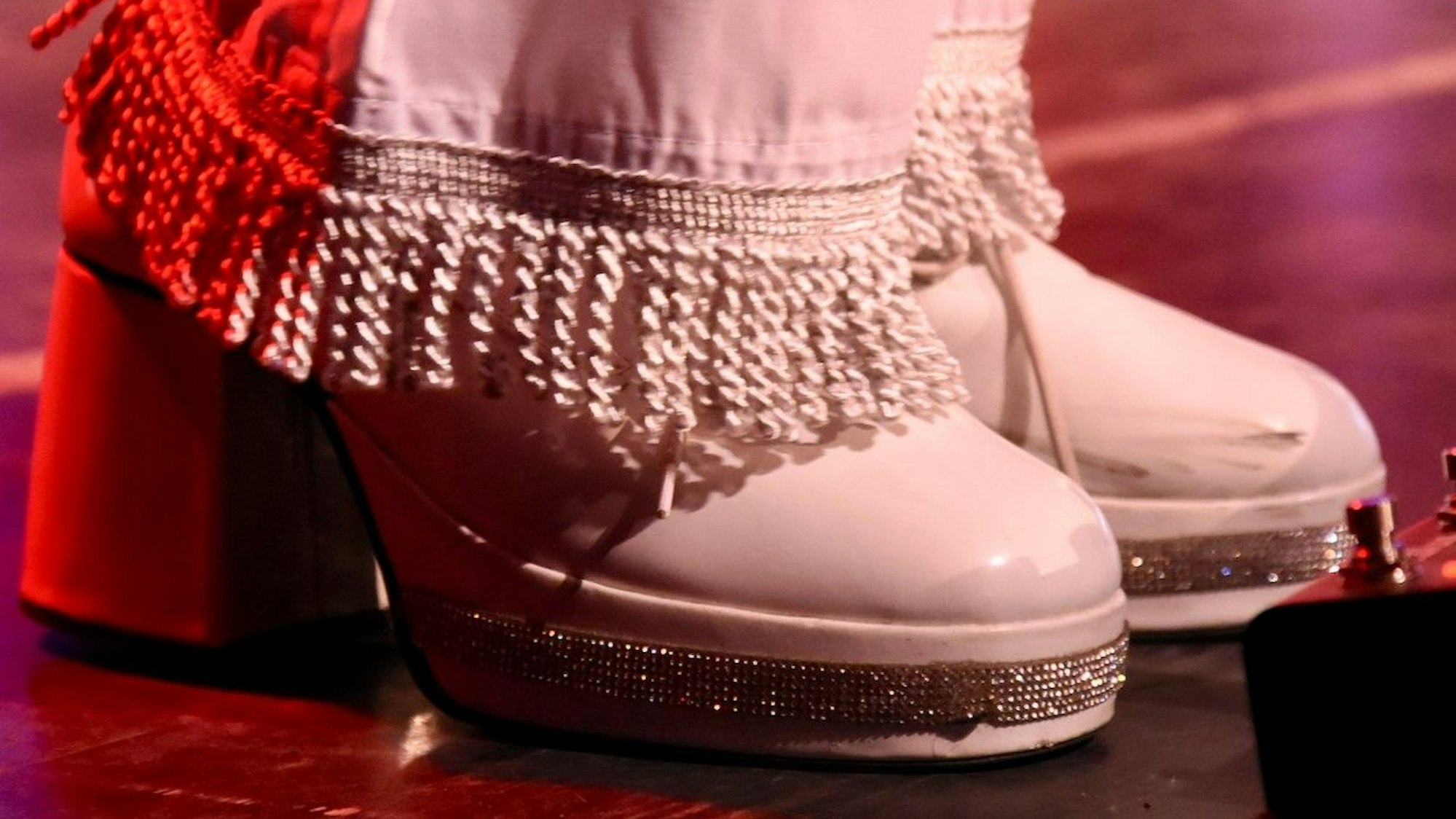 Nahaufnahme von weißen Schuhen mit Glitzerrand und hoher Plateausohle.