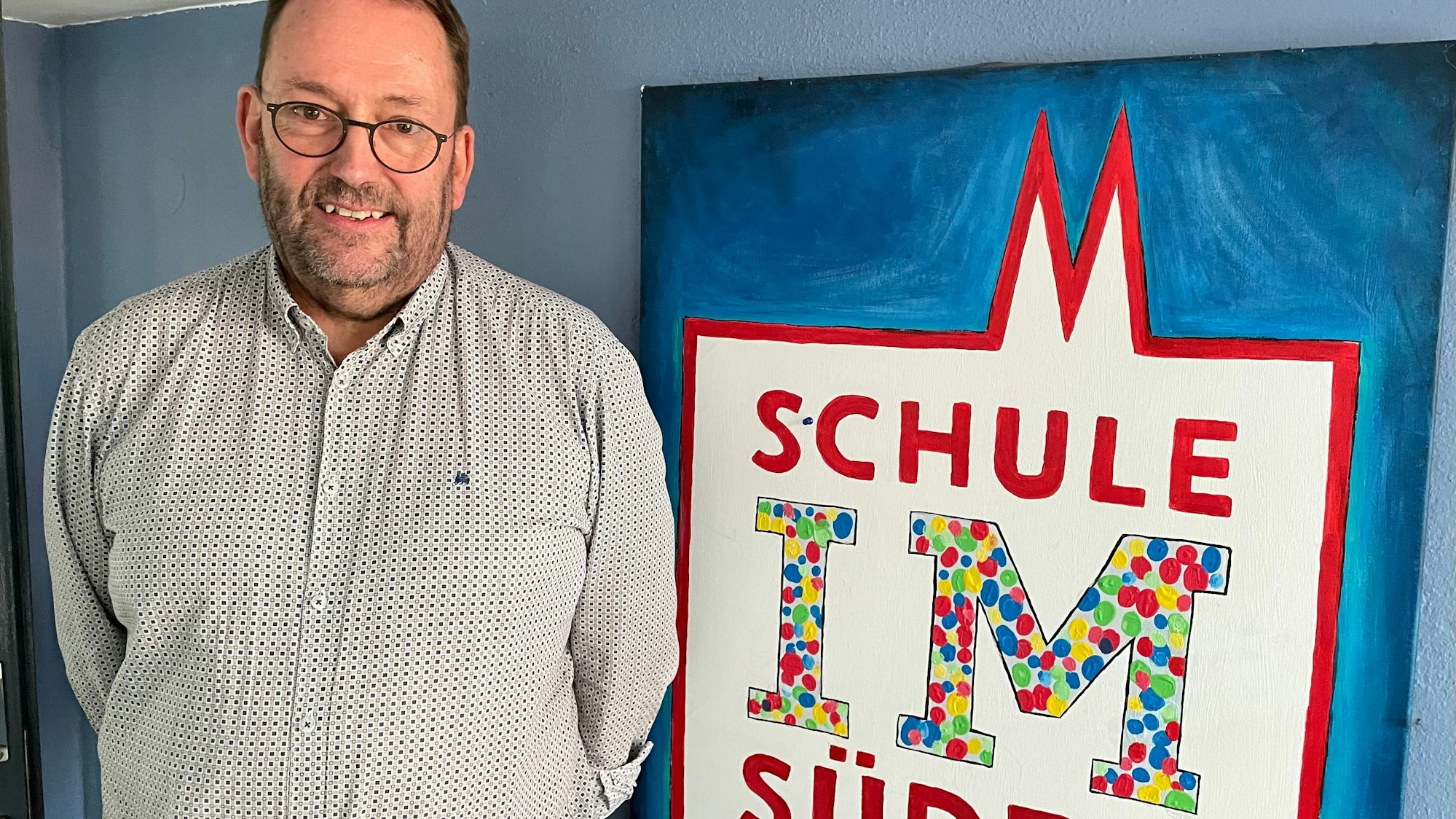 Ein Mann steht vor einem Plakat mit dem Namen der Schule IM Süden.