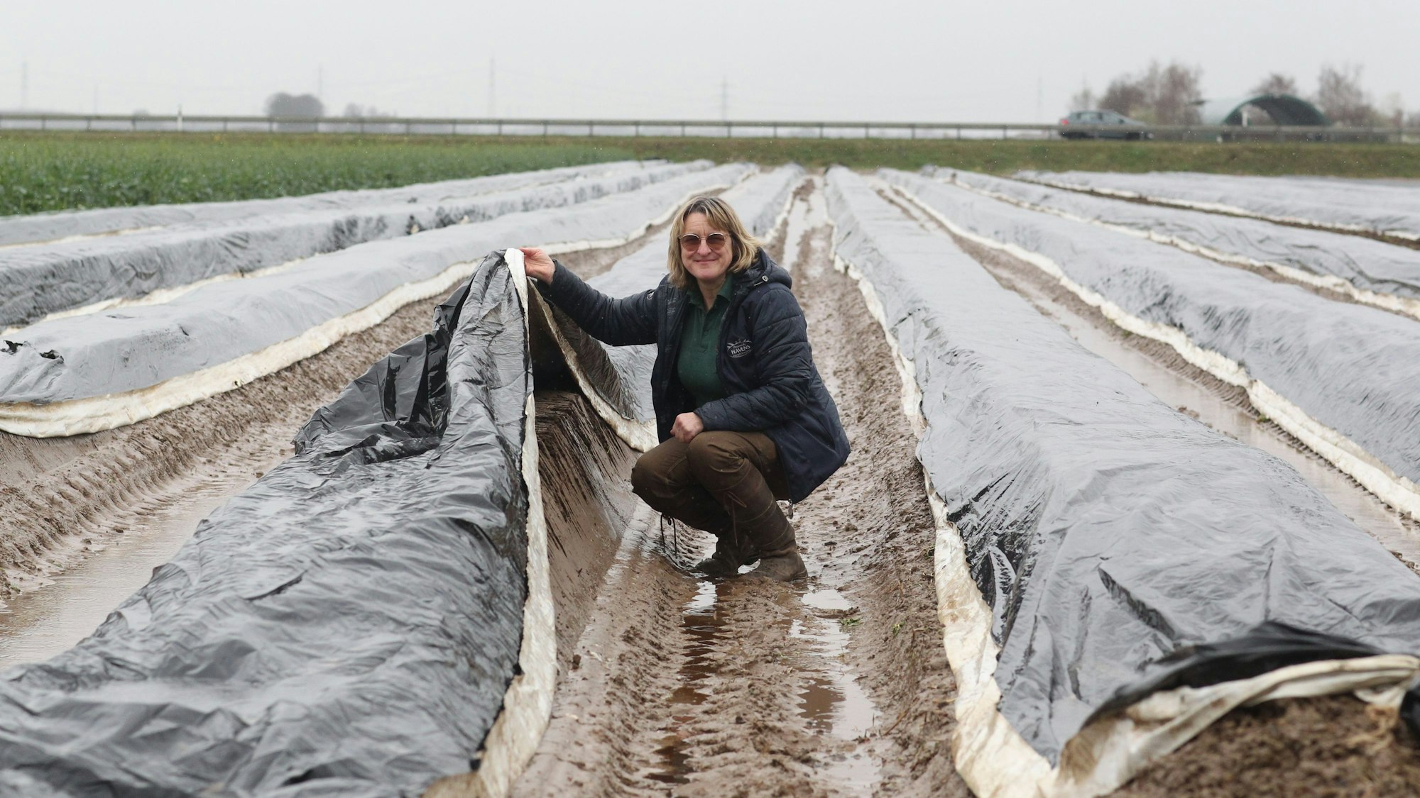 Eine Frau kniet auf einem Spargelfeld.