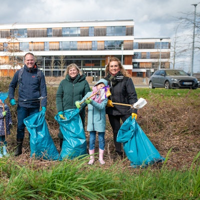 Männer, Frauen und Kinder mit Papiersammelzangen und blauen Müllsäcken hinter der Gesamtschule in Hermülheim.