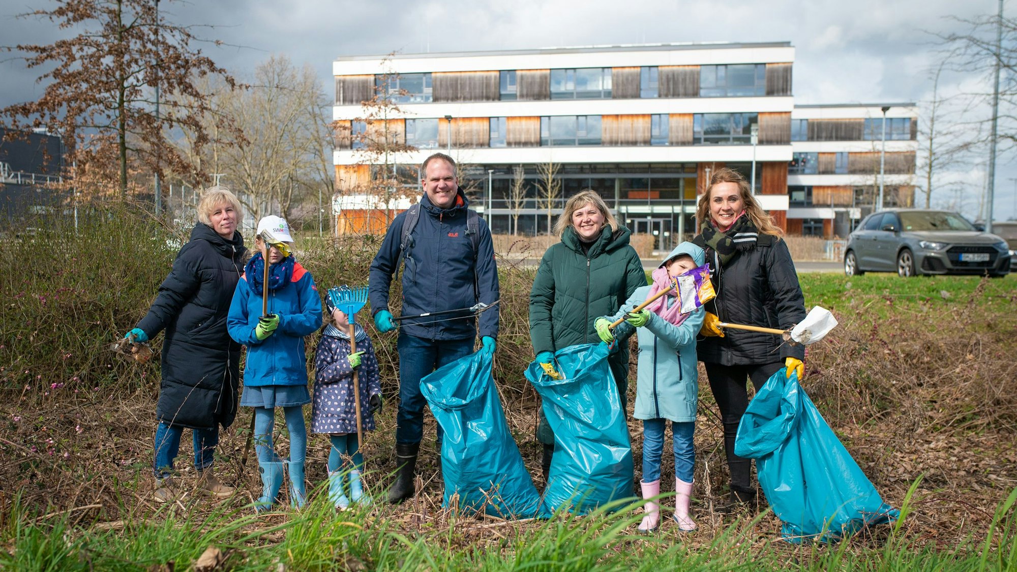Männer, Frauen und Kinder mit Papiersammelzangen und blauen Müllsäcken hinter der Gesamtschule in Hermülheim.