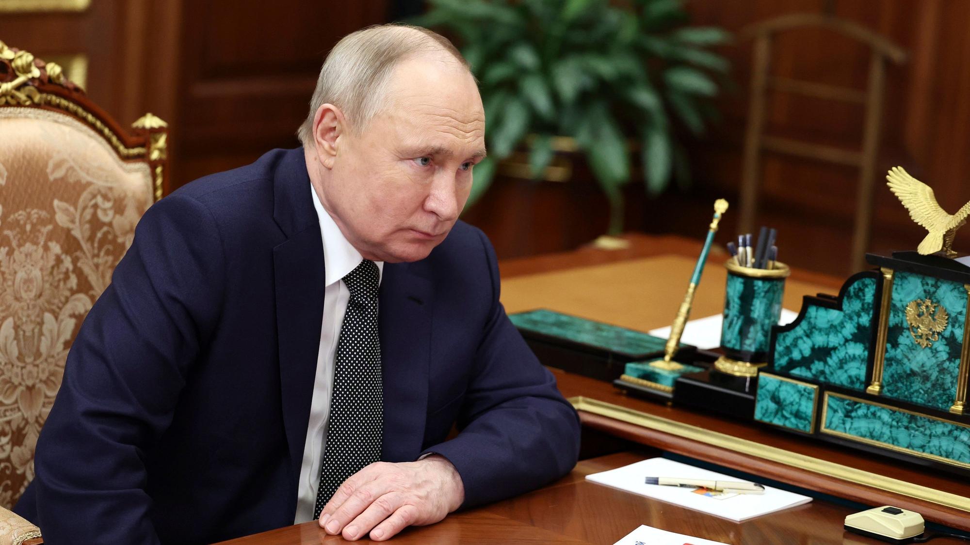 Russlands Präsident Wladimir Putin sitzt in seinem Büro im Moskauer Kreml und hört bei einem Gespräch zu. Er trägt einen blauen Anzug und Krawatte.