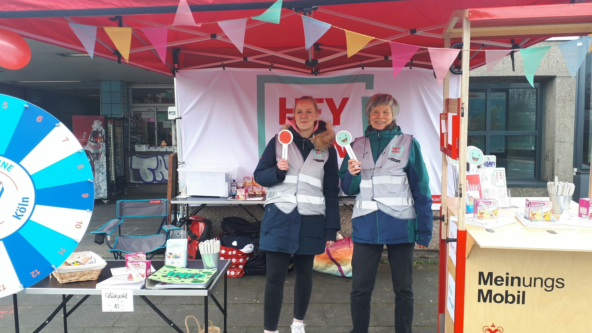 Unter der Plane eines Stands stehen zwei Frauen mit Smiley-Zeichen.