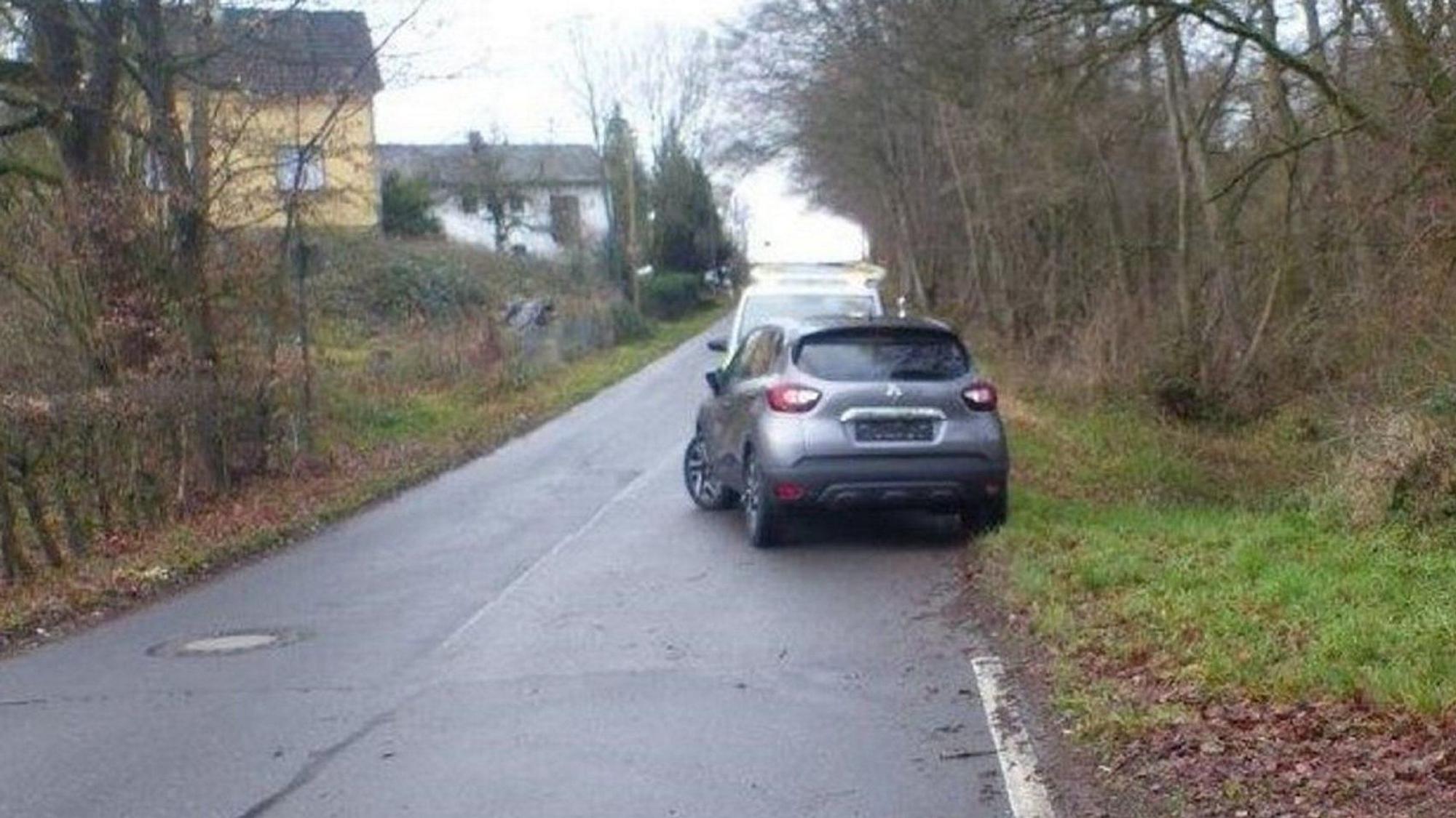 Ein Wagen steht an einer schmalen Straße halb auf der Fahrbahn.