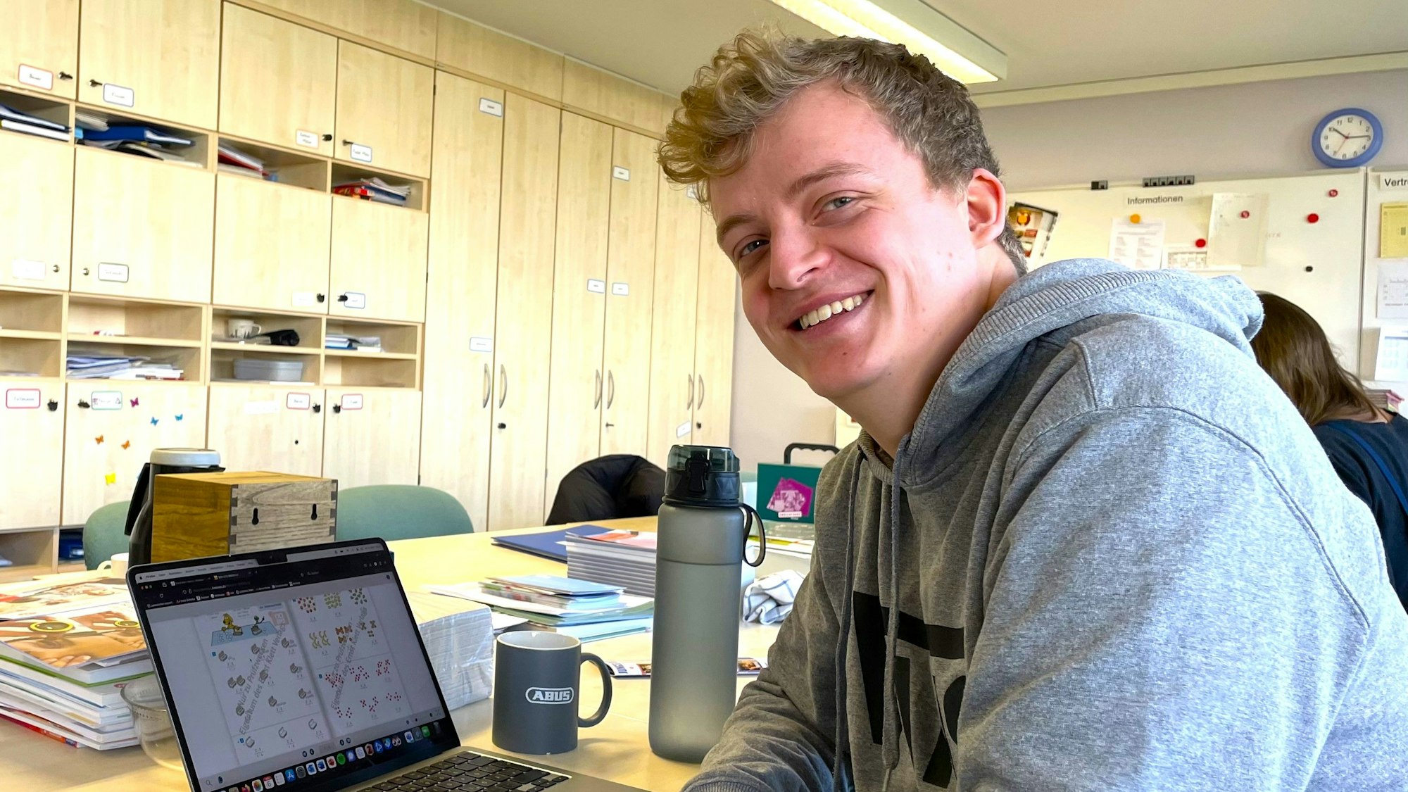Ein junger Mann sitzt an einem großen Tisch in einem Lehrerzimmer.