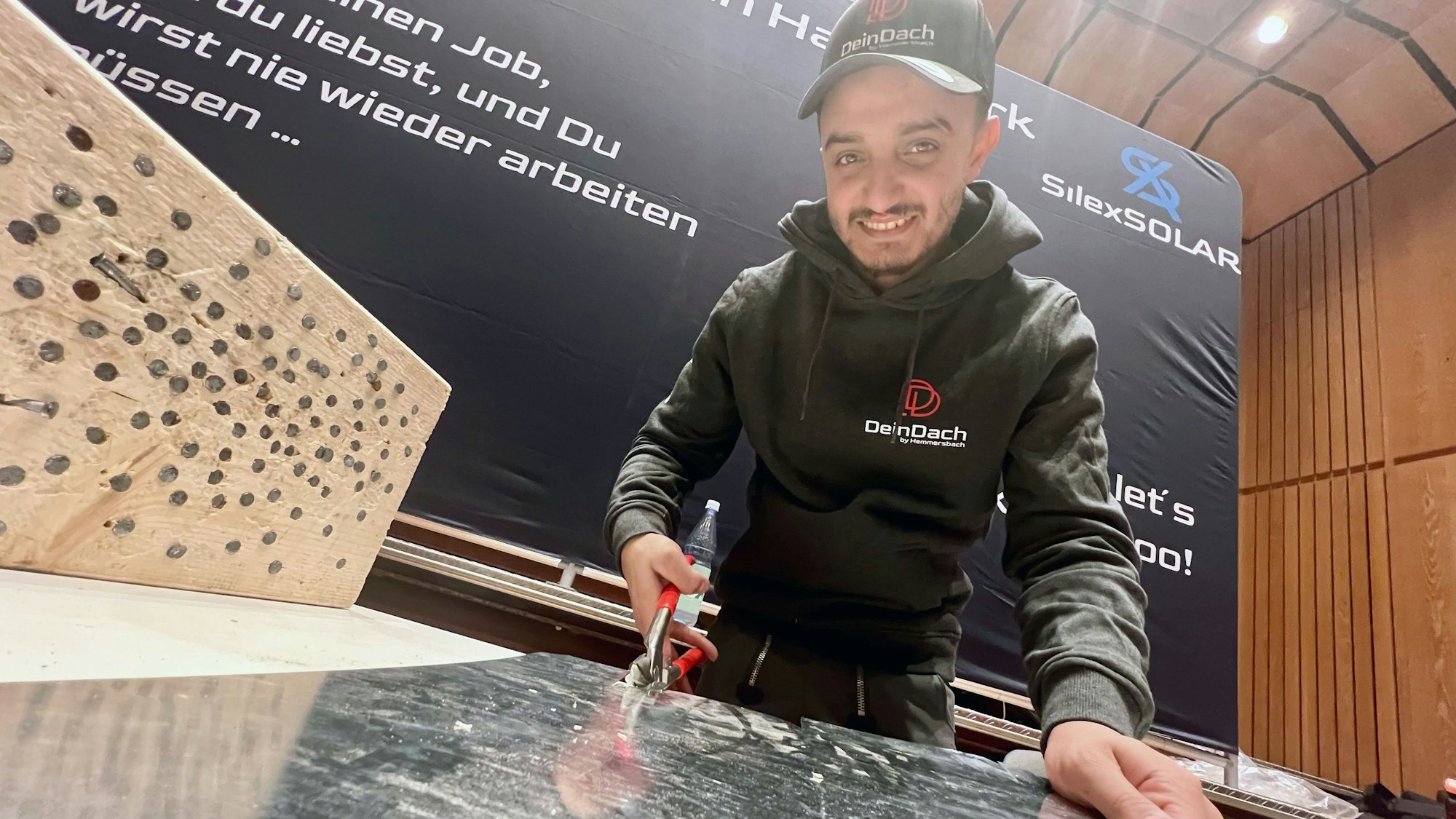 Ein junger Mann mit Kappe und Hoodie schneidet Blech an einem großen Tisch.