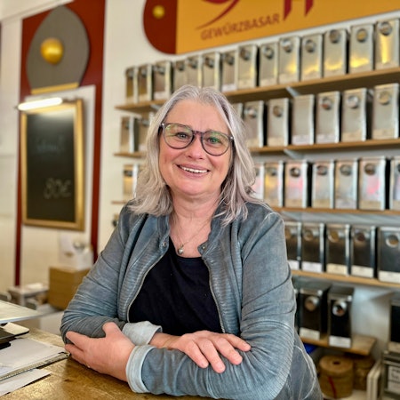 Eine Frau mit schulterlangem Haar und Brille schaut lachend in die Kamera.