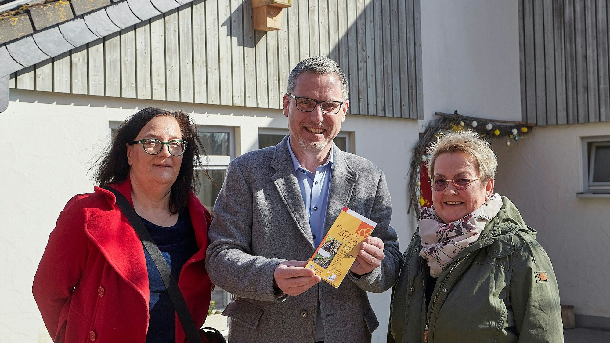 Brigitte Wies, Norbert Crump und Iris Beging (von links) stehen vor einem Gebäude, Crump hält ein Heft im DIN-Lang-Format in der Hand.