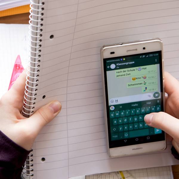 Eine Schülerin sitzt mit ihrem Handy und ihren Schulsachen an einem Schreibtisch.