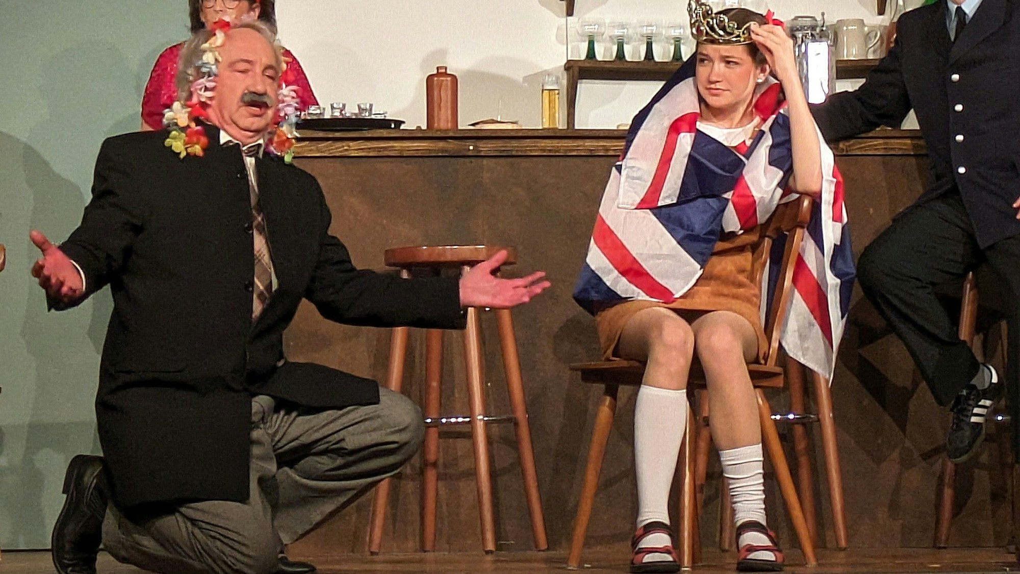 Freistaatpräsident Roland Tsatziki (Martin Schumacher), erklärt seiner Enkelin Greta (Kira Muß), was er bei seinem Staatsbesuch in England mit der Queen erlebt hat.