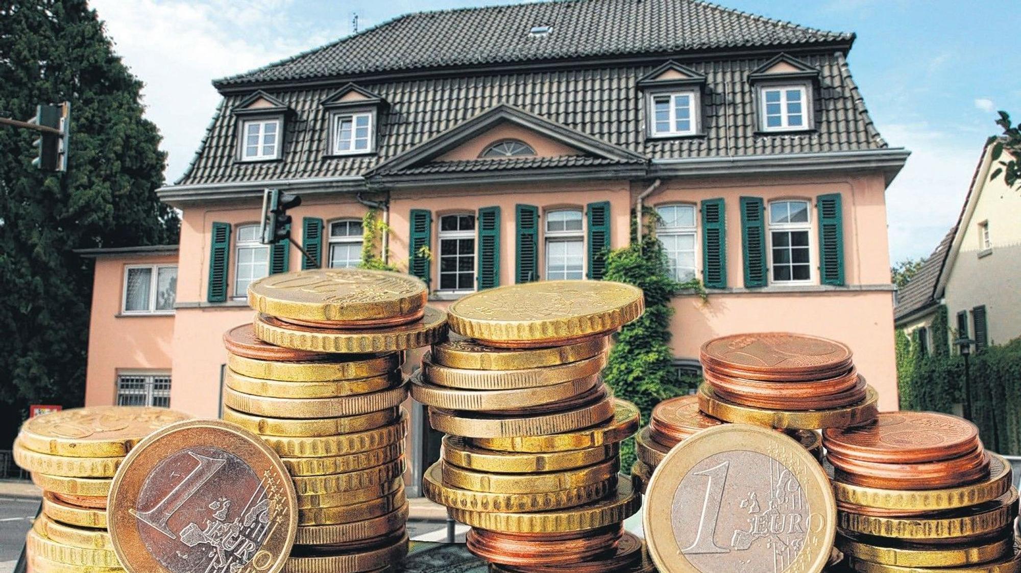 Ein rosafarbenes historisches Rathaus, davor Stapel Euromünzen.