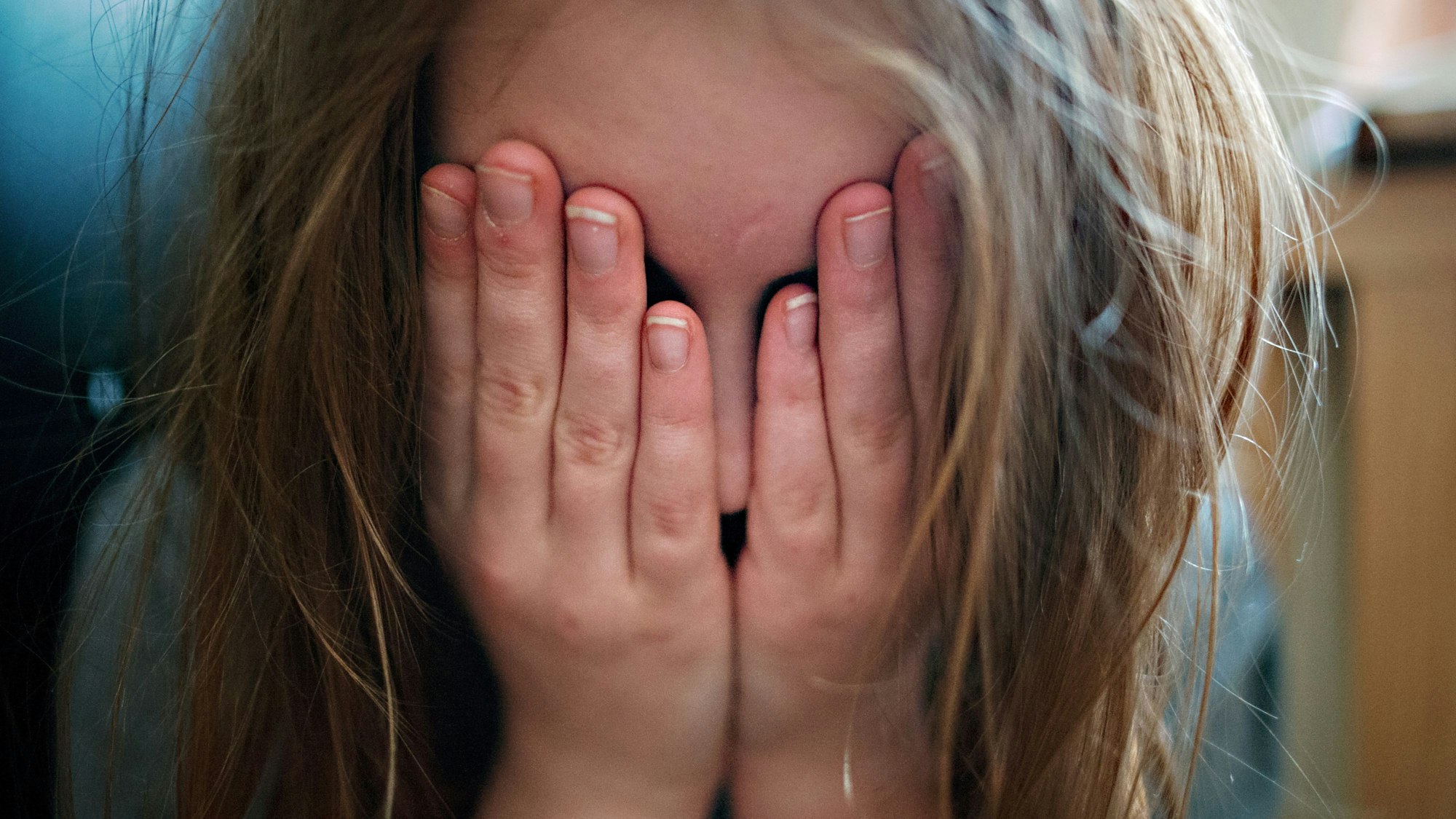 Ein junges Mädchen hält sich die Hände vor ihr Gesicht.